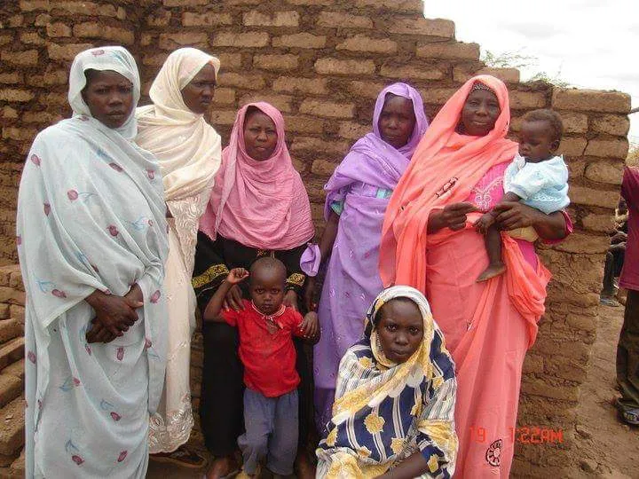 Women and children standing in front of a mud-brick wall in Sudan